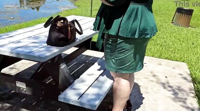 Voluptuous woman in green dress toys with a black dildo on a public bench
