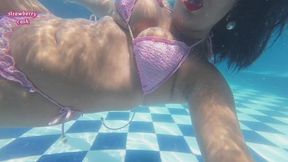 Blowing bubbles in the swimming pool in a pink bikini