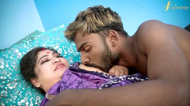 Tattooed Asian woman takes a blonde-haired black man deep inside on a bed against a blue wall