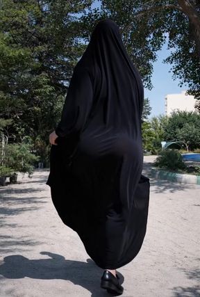 Middle Eastern woman in black burka walking on sidewalk