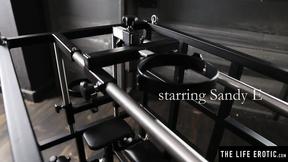 ”Kinky blonde Sandy E fingers her beaver in a BDSM cage”
