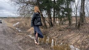 girl in high-heeled shoes walks along a wet and dirty road, dirtying her shoes and stockingsR