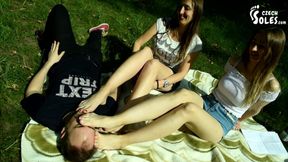 Two barefoot girls in park having their feet worshiped by a stranger