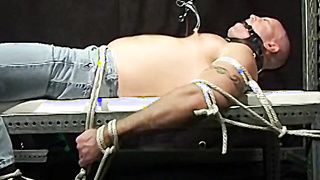 Muscular Bigg Pete can only moan in agony through his gag as his big nuts are pulled