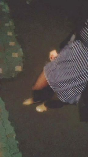 A girl in black stockings with beautiful legs walks down the street at night, showing an anal dildo remote control under skirt