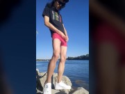 Twink boy with long dark hair pissing pee on the river dressed in glasses cap sneakers boxer tshirt