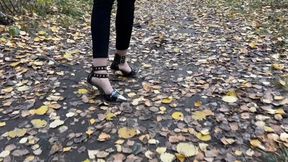 A girl in high-heeled shoes walks through the forest where there is a lot of dirt, she gets her heels dirty and enjoys it