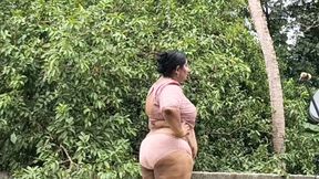 A full-figured woman in a white skirt and pink top strips down and walks nude outside.