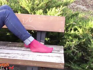 Barefoot brunette hair takes off stockings, shows feet in a park