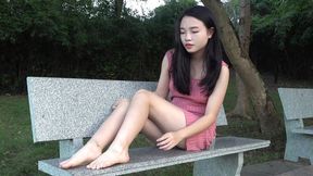 Girl in pink dress showing her feet on park bench