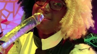 Dark-skinned woman with glasses takes a glossy dildo deep while bent over a stool