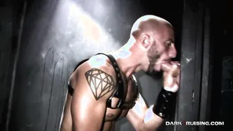 Muscular tattooed guy sucks big cock through glory hole