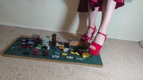 Giantess Lily Kink toy car crush of tiny cars, buses, trucks & buildings in big mega red heels and stomping the bits in a box high right view
