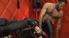 Executive turned leather man works over bound and gagged executive.