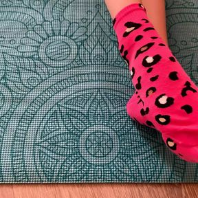 Gloria Gimson in pink socks caresses her feet on a yoga mat