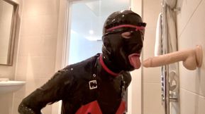 Latex Alice blows and deep throats a dildo while on her knees in the bathroom