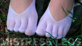 Goddess feet in soft white socks and jeans on a sunny grassy field