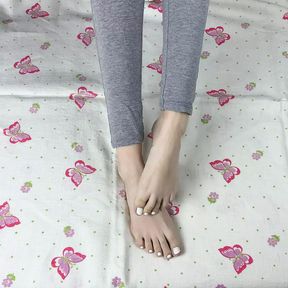 Girl in gray leggings with long legs caresses her feet with a white pedicure