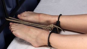 Topless tapegagged barefoot Alina, cuffed with strict handcuffs by hands and feet, stretched on the bed between headboard and footboard, is trying to ease her position (HD MP4)