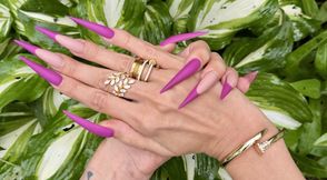 New purple color Long nails, sharp stilettos, palms, long fingers in the garden with flowers