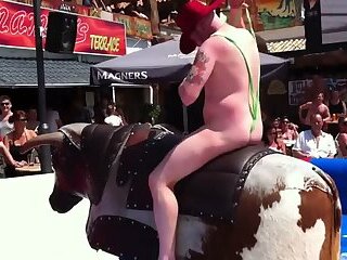 Guy Riding A Mechanical Bull With His Male Parts Popping Out Of His Mankini