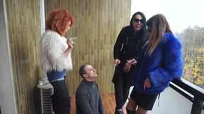 Fur-clad Femdoms Dominate Submissive on Balcony