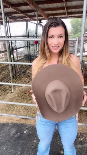 Woman holding cowboy hat in front of barn